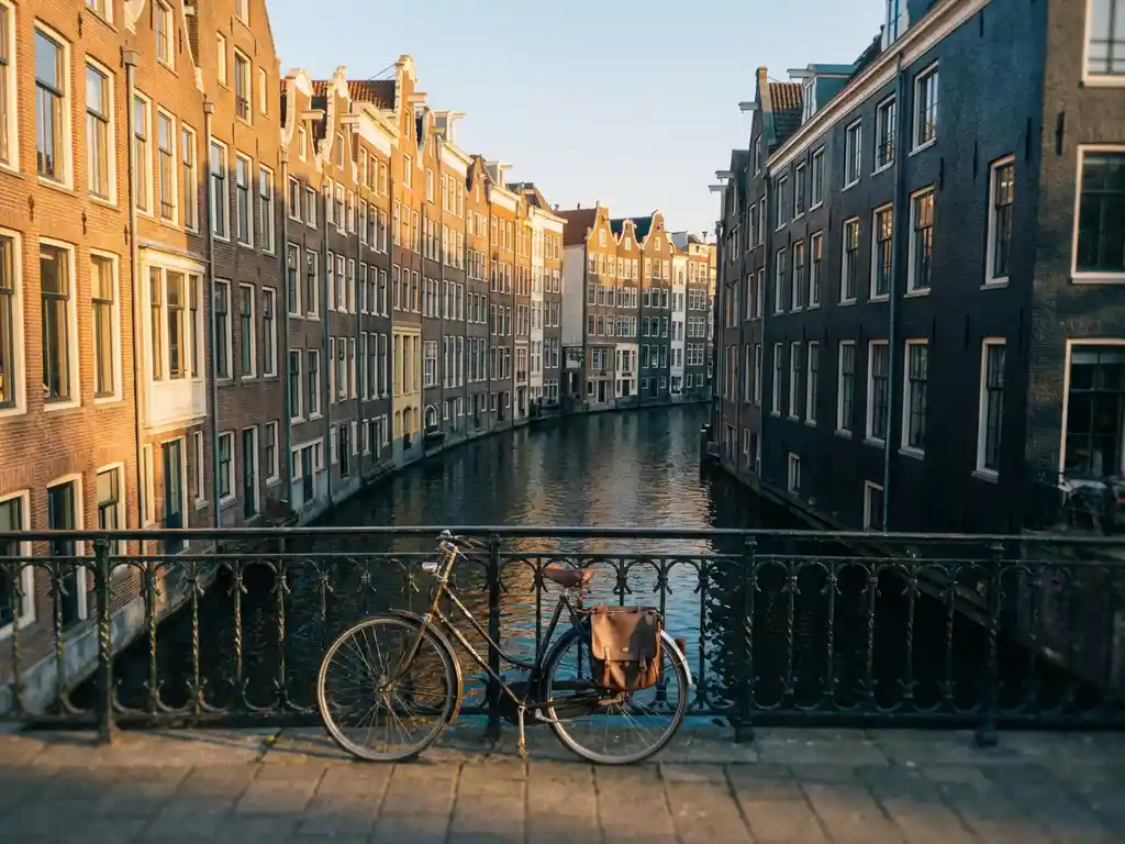 Luchtfoto van smalle Amsterdamse gracht met gevels in gouden middagzon, fiets tegen sierlijk ijzeren hek op de voorgrond.