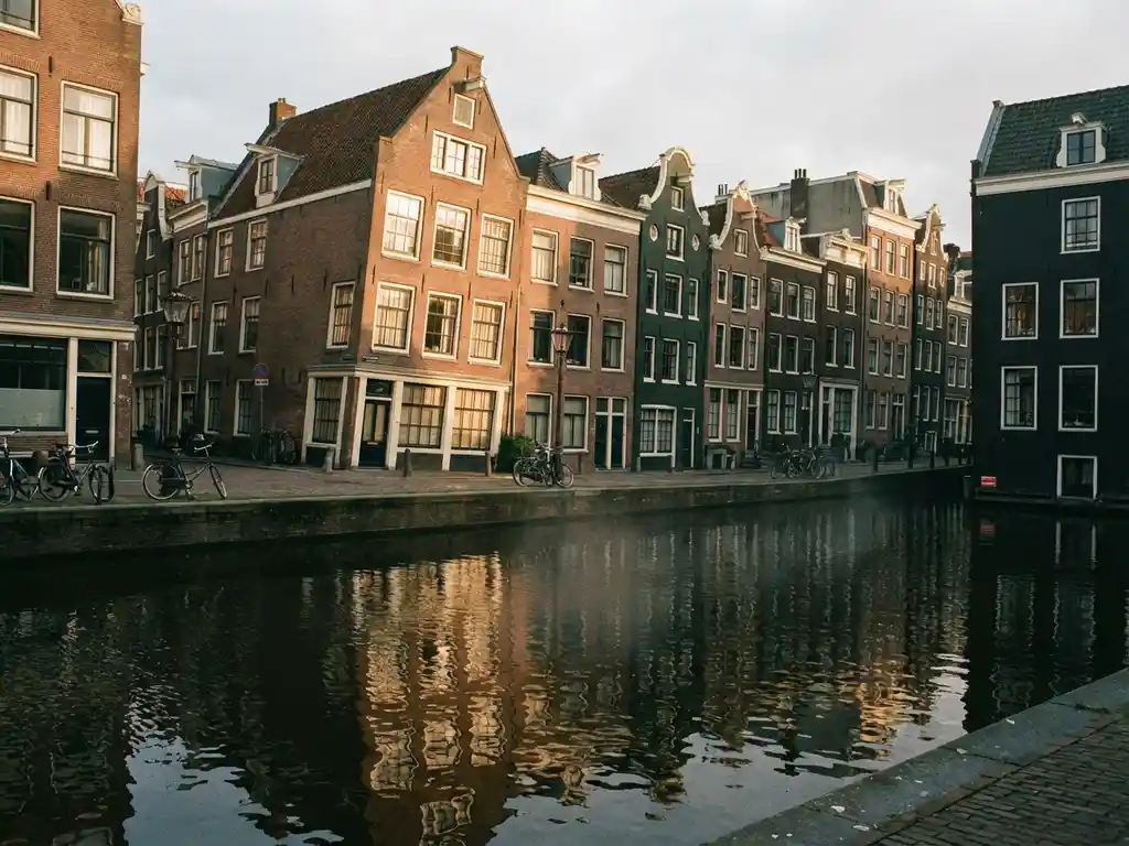 Scheve grachtenpanden in Amsterdam weerspiegeld in donker, rimpelend water, smalle bakstenen gevels in terracotta en groen.