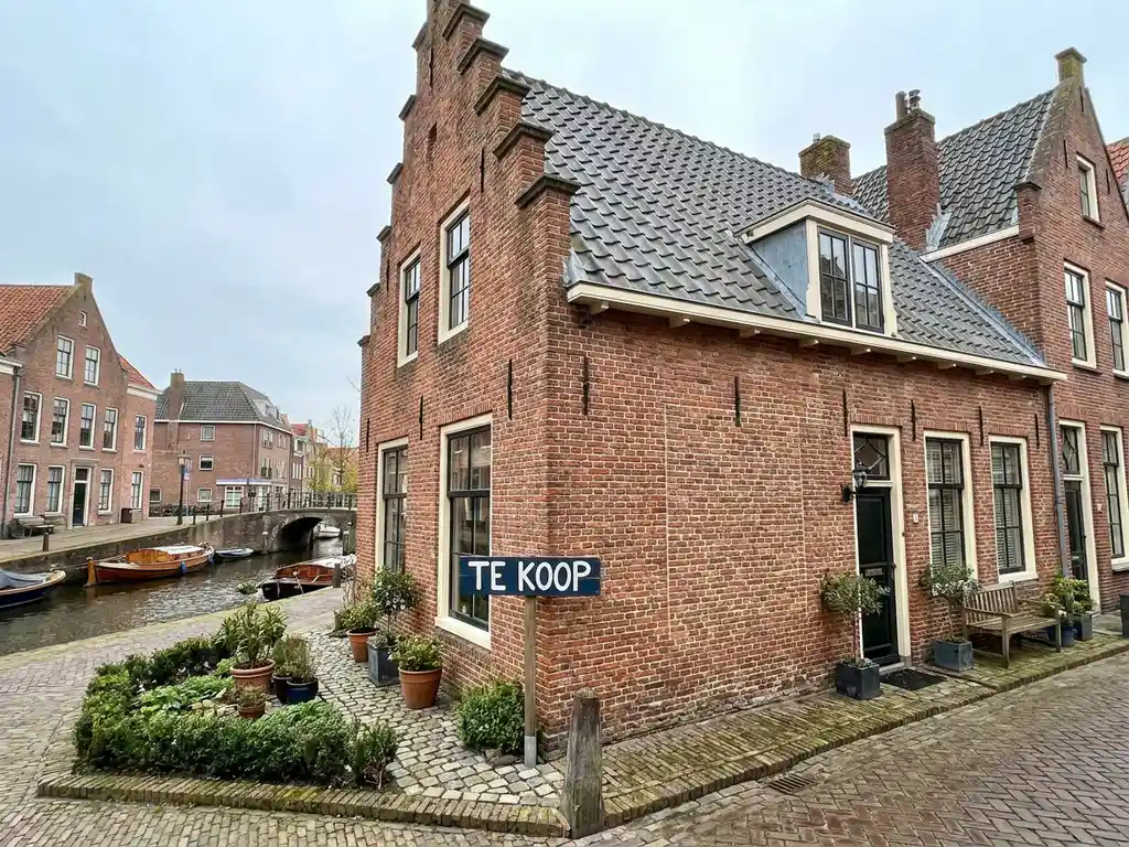 Hollandse bakstenen rijtjeswoning in Alkmaar te koop, met traditionele trapgevel en bordje in de voortuin, rustige gracht op de achtergrond.