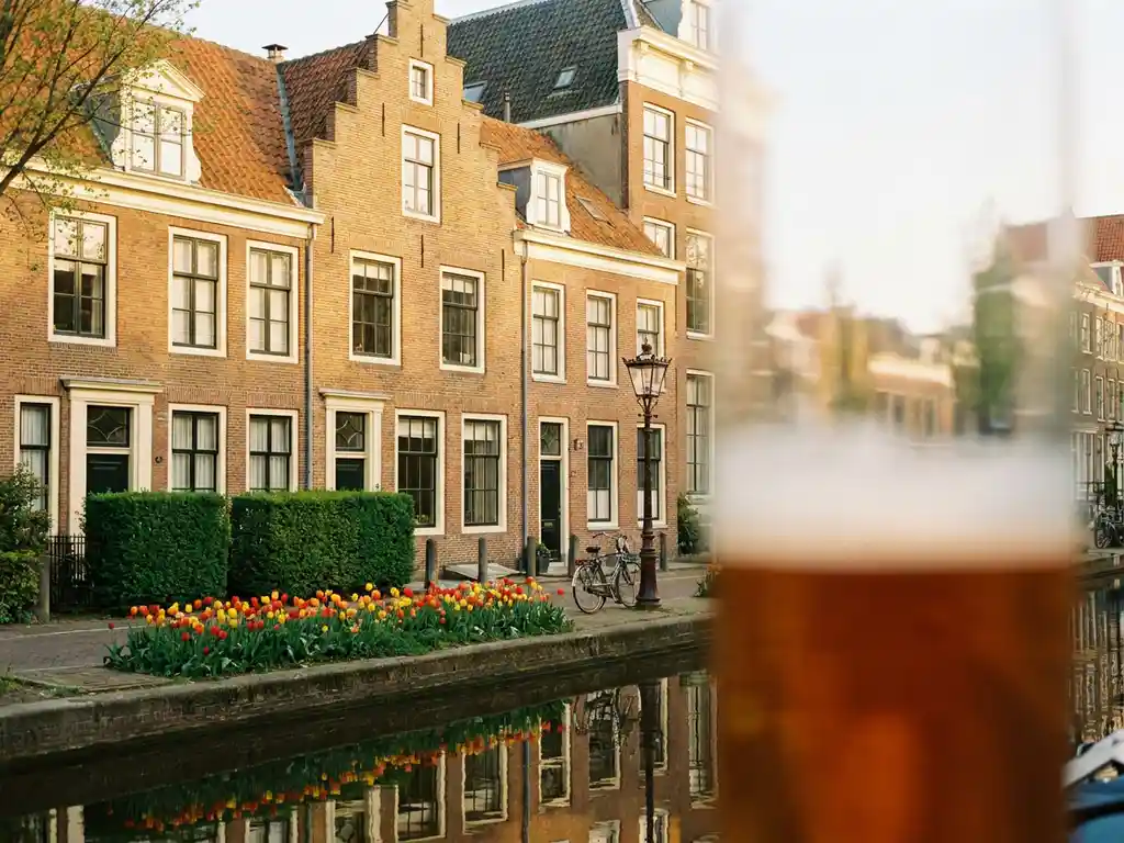 Hollands grachtenpand met bakstenen gevel, witte kozijnen, bloeiende tulpen en kalm kanaaalwater in ochtendlicht.